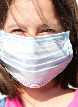Extreme close up of a smiling little girl with surgical mask for protection against the Corona Virus during the lockdownの写真素材