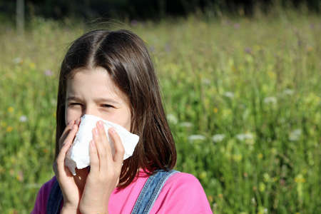young girls blows her nose with a white handkerchief because she has allergy to Pollen on the field in full bloomの写真素材