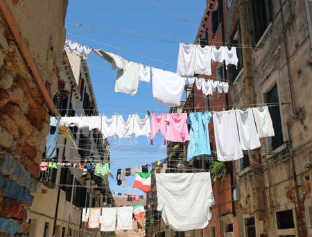 many clean clothes hanging out to dry in the sun and an Italian flag in the historic city centerの写真素材