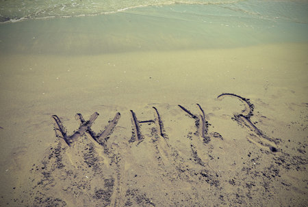 Big text WHY written in the sand of the beach by the sea with question mark