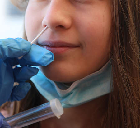young girl makes a medical swab for positivity research and gloves of doctor with test tube for medical analysisの写真素材