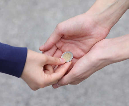 hand of the young woman while giving alms with a coin to the poor boyの写真素材