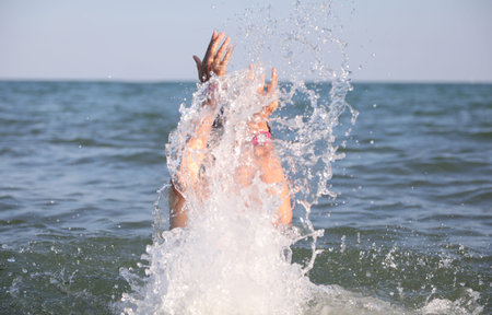 young little girl splashes the sea water playing and having fun during the summer vacation