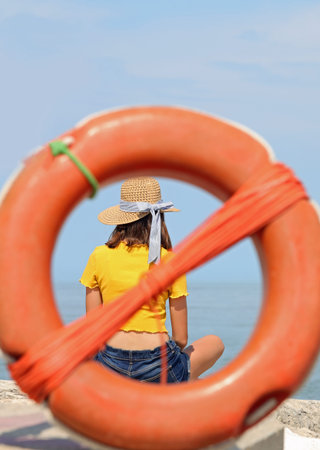 young skinny girl with straw hat and yellow t-shirt inside an orange plastic life buoy