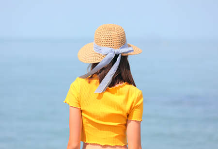 young skinny girl with straw hat and yellow t-shirt and the sea in the background in summerの写真素材