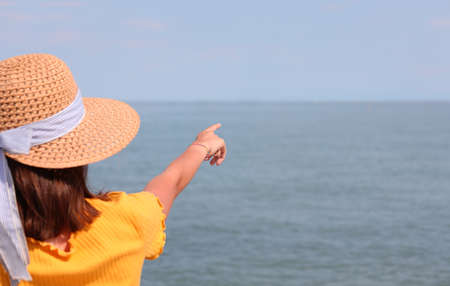 girls with straw hats points to a point on the horizon on the calm seaの写真素材