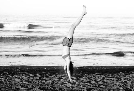 young athletic girl during a calisthenics with legs up on the shore of the beachの写真素材