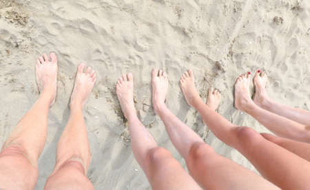 legs and feet of a family of four on the sandy beach in summerの写真素材