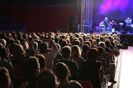 crowd of excited people cheering during an indoor concert with the band on stageの写真素材