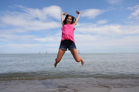 slender young girl takes a very high jump and is very happy by the sea in summerの写真素材