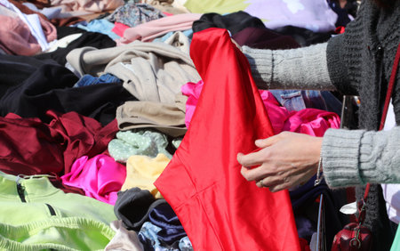 hands of women trying a red dress in the stall with many items of clothing for sale in the marketの写真素材