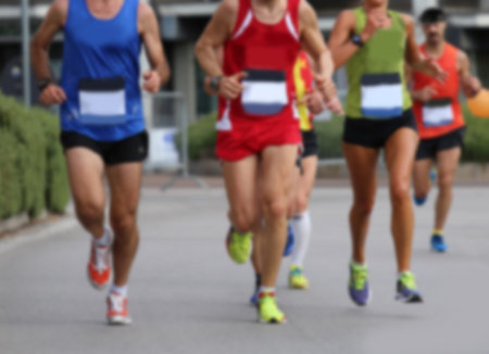 Intentionally blurred group of athletes runners during foot race in the city on the asphalt road...