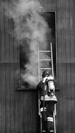 firefighter in action in the fire station with self-contained breathing apparatus and oxygen cylinderand the thick smoke coming out of the windowの写真素材