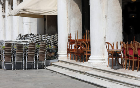 many chairs and table of the outdoor cafe piled in the square without people during the economic crisis caused by the lockdownの写真素材