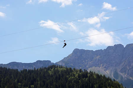 fearless person hanging from the steel cable that connects the opposite slopes of the mountain and the force of gravity that drags down and mountains in backgroundの写真素材