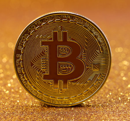 Golden Coins with the symbol B in capital letters symbolizing the cryptocurrency called BITCOIN on a shimmering backgroundの写真素材