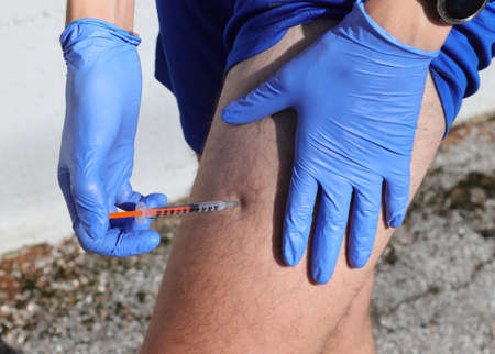 young boy giving himself an insulin injection due to diabetes on the thigh of his leg with blue glovesの写真素材