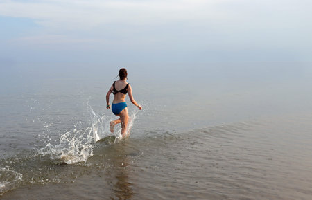 young girl during the run in the middle of the sea water in the summer with sports clothing
