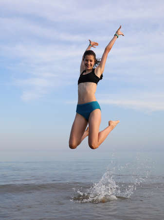 joyful young slender teenage girl jumps for happiness on the seashore in the summerの写真素材