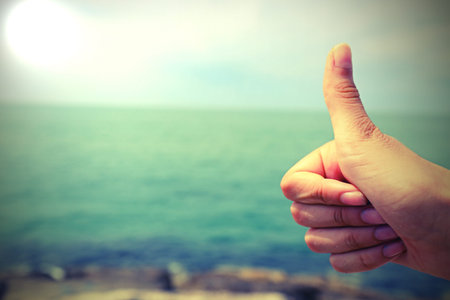 thumb up of young hand by the sea symbol of positivity and that all is well with old toned effect