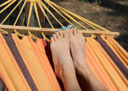 barefoot feet of a young girl while resting in the hammock in the park in summerの写真素材