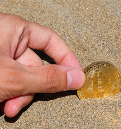 hand of man finding a golden coin with the capital letter B symbolizing the crypto currency Bitcoin on the sand of the beachの写真素材