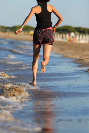 slender athletic girl running barefoot on the seashore in summerの写真素材
