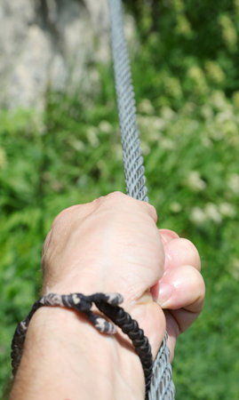 hand of the person holding firmly the rope of the via ferrata in the mountains during the hike