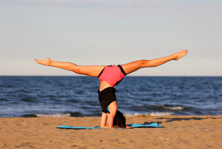young slender athletic girl does exercises on gym mat on the beach in summerの写真素材