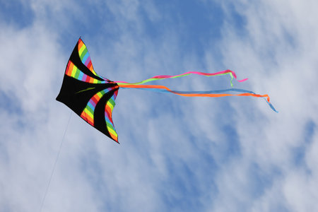big kite with black color and many colors of the rainbow flying high attached to a stringの写真素材
