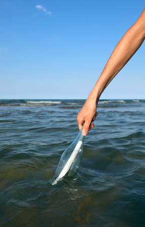 hand of the boy who collects from the sea the bottle with a secret messageの写真素材