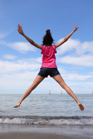 happy girl jumping and rejoicing for joy by the sea in summerの写真素材