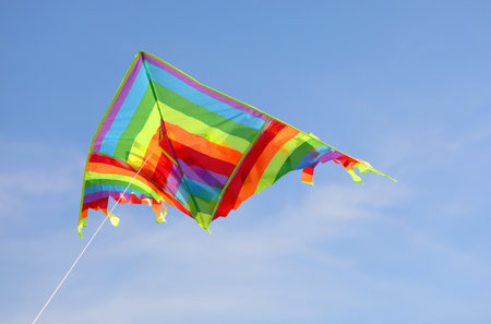 colorful kite flies high in the blue sky tied to a stringの写真素材