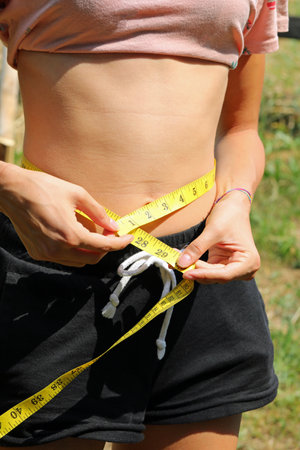 skinny teenager girl measuring her waist with a measuring tapeの写真素材
