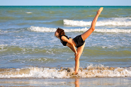 girl does gymnastic exercises on the sandy beach by the sea in summerの写真素材