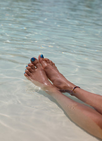 long legs of girl with feet with colorful nail polish in tropical waterの写真素材