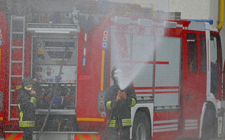 firefighters with the fire truck while extinguishing fire with a powerful jet of extinguishing...