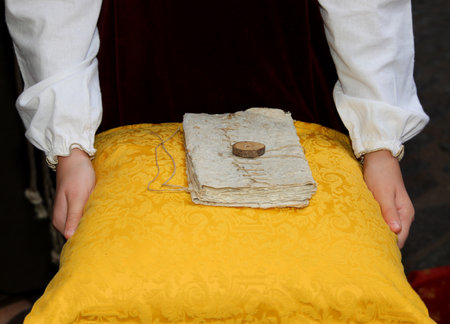 parchment closed with string and seal on a soft yellow cushion carried by the hands of childの写真素材
