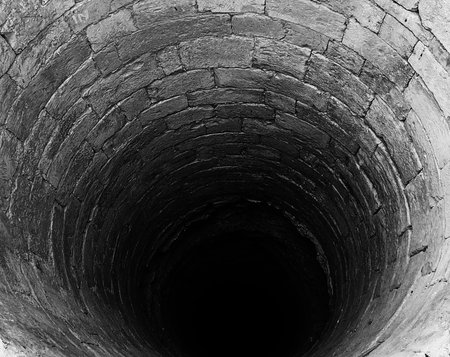 narrow tunnel or a bottomless pit made of rocks and stones in black and white