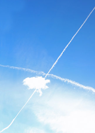 long white trails high in the blue sky crossing a cloud without airplanesの写真素材