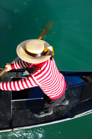 Venetian gondolier with hat rowing on gondola boat on the water of grand canal in Venice in Italyの写真素材
