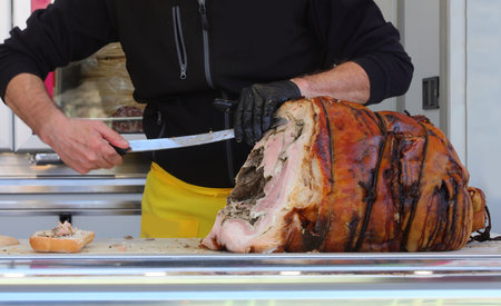gloved hand of a deli worker slices roasted porchetta with a large knifeの写真素材
