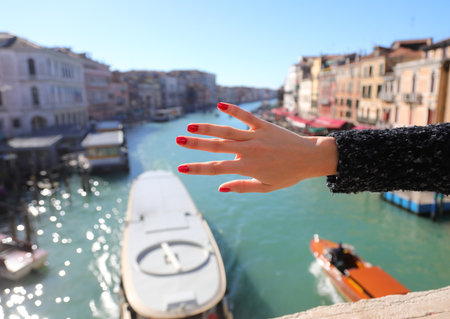 Five fingers of the hand of the young girl with nails with red nail polish and the Grand Canal in Venice ITALYの写真素材