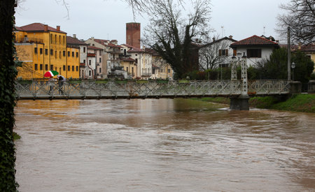 Raging river during flooding with risk of overflow and nearly submerged pedestrian iron bridgeの写真素材