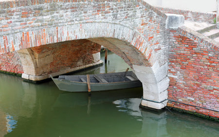 Ancient Venetian-style brick bridge with a boat underneath in a navigable canalの写真素材
