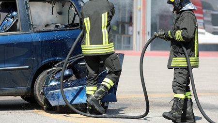 firefighters with helmets extinguish the fire of the wrecked car after the car accident with the big...