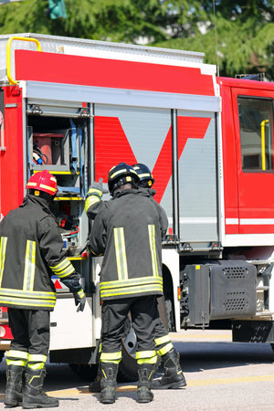 three firefighters take specialized rescue equipment from red fire engine