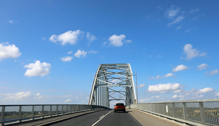 asphalt road with a large metal truss bridge and a car crossing itの写真素材