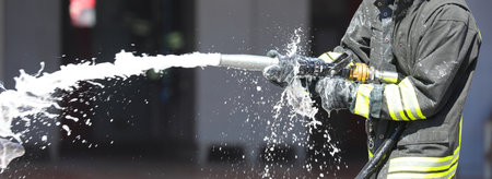firefighter is spraying foam extinguishing agent with a powerful hose to control a fire during an emergency situationの写真素材