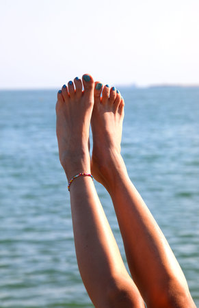 Long legs with bare feet by the blue sea in the warmth of summer